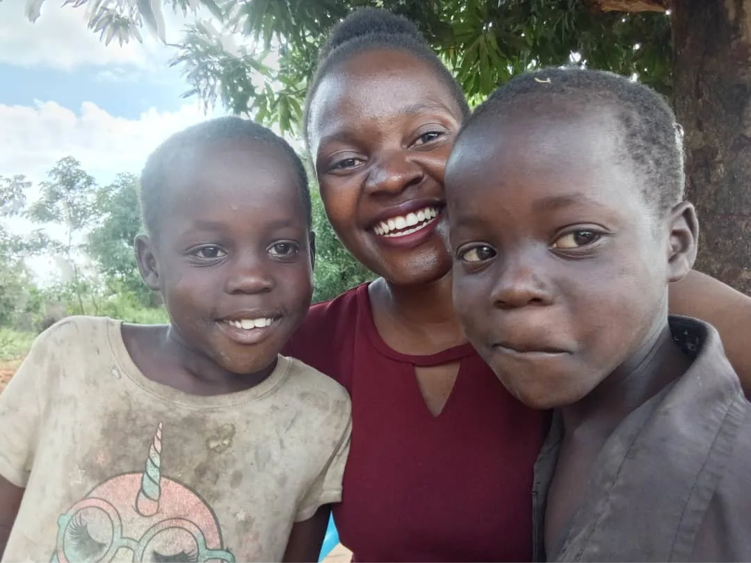 Shining Light Uganda team member smiling with two children