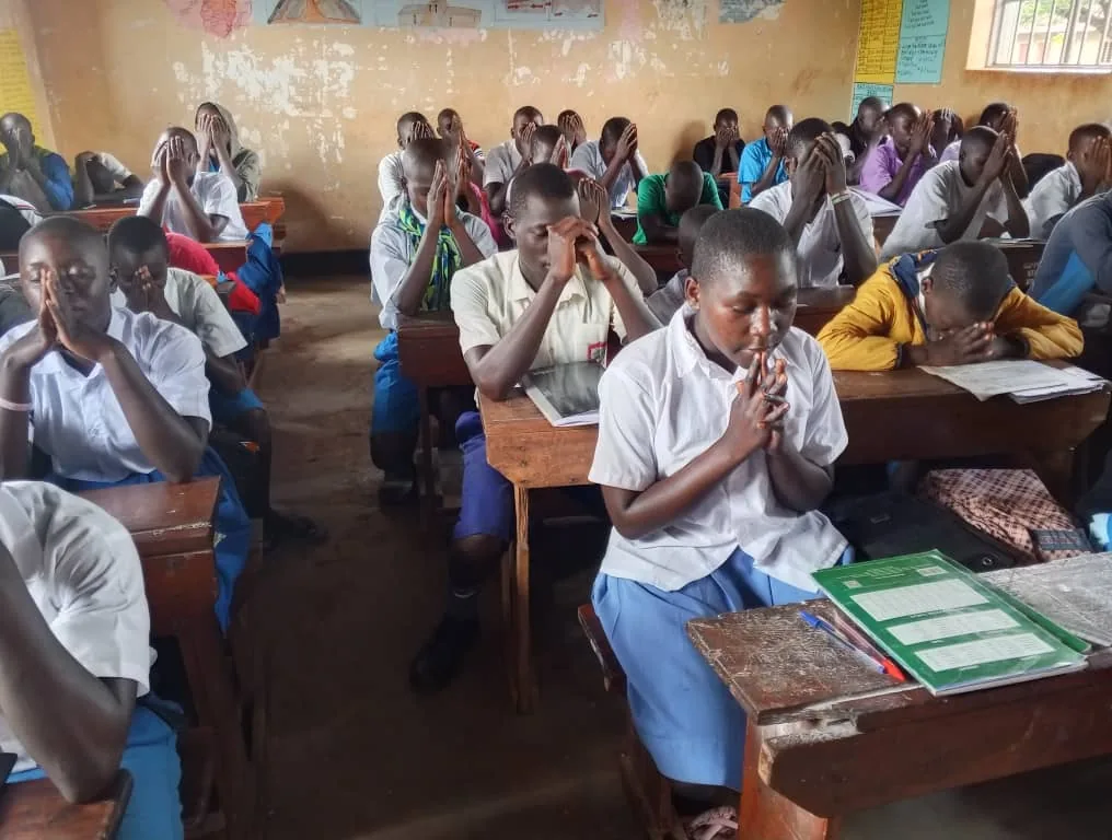 Pupils praying together at their desks during a classroom discipleship session