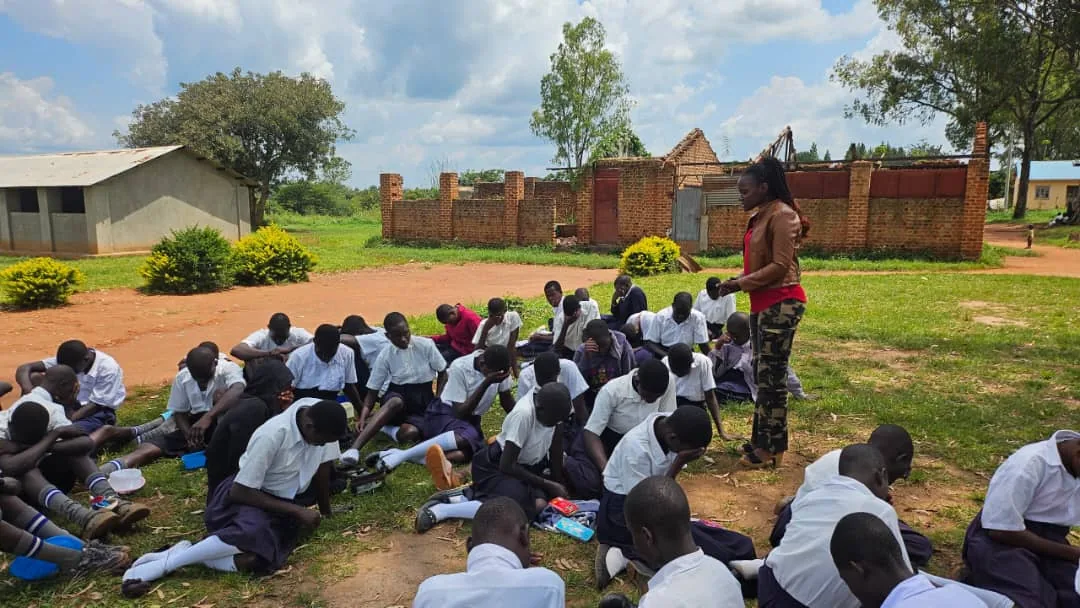 Pupils seated on the ground while a facilitator leads a school outreach session