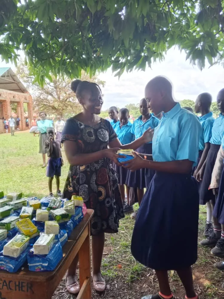 Team member handing sanitary pads and soap to a schoolgirl at a distribution table