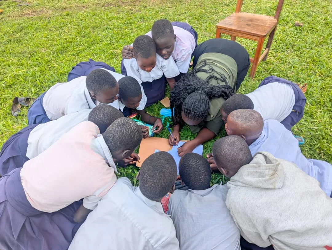 Children gathered closely around a facilitator writing together on the grass